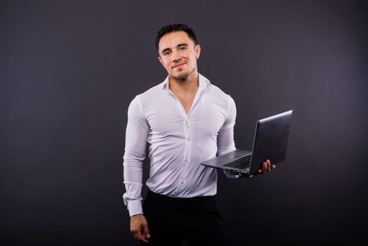 Image of a young cheerful businessman holding and using laptop isolated over dark background