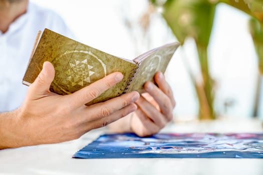 Studying Rules of Leela: Man Holds Book with Game Instructions in Hands, Close-Up of Hands Against Background of Playing Field, Turkey, Alanya - April 14, 2024