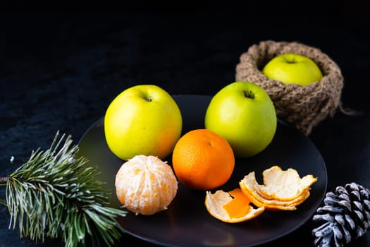 Green apples tangerines and pine cones on a table, dark background