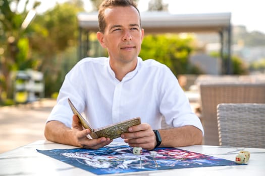 Instructions for Game of Leela: Man Holds Book in Hands, Against Playing Field Background, Portrait of Man Studying Rules, Turkey, Alanya - April 14, 2024