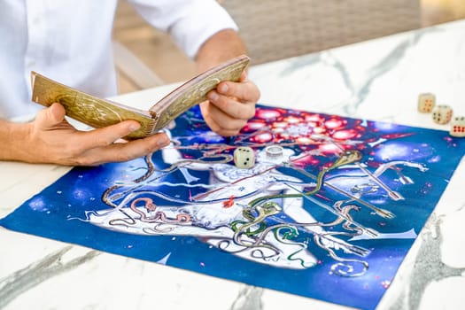 Close-Up of Hands Holding Book with Game Instructions for Leela, Man Studying Rules Against Background of Playing Field, Turkey, Alanya - April 14, 2024