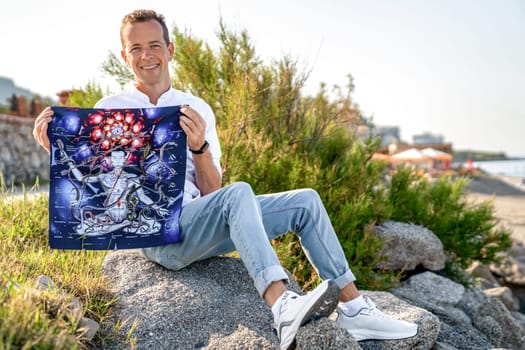 Turkey, Alanya - April 14, 2024. Man Holds Expanded Playing Field of Ancient Indian Board Game Leela in Hands While Sitting in Nature Park