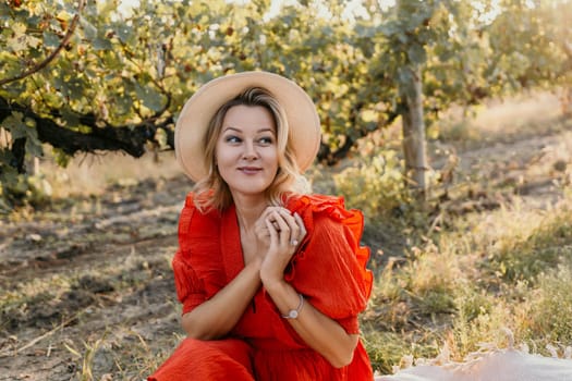 A woman in a red dress is sitting in a field with a straw hat on. She is smiling and looking up at the sky