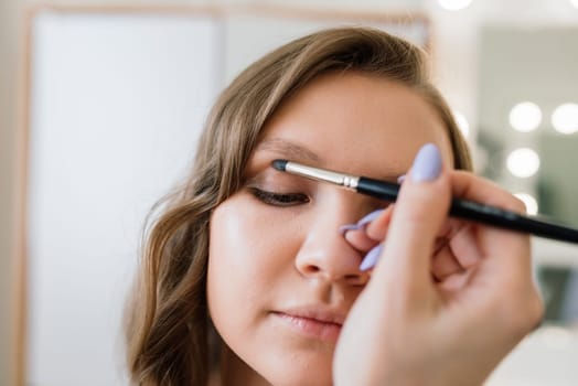 Makeup artist applies lipstick. Hand of make-up master, painting lips of a young beauty model.