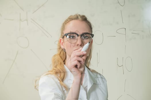 A Caucasian woman in a medical gown thinks and finalizes formulas on a transparent wall