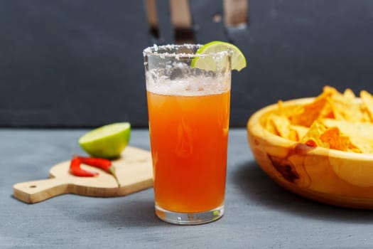 Michelada cocktail with tomato juice, beer and lime in a glass and nachos. Selective focus