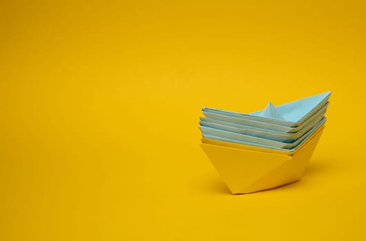 Paper boats on a yellow background, representing the concept of unity and achieving common goals.