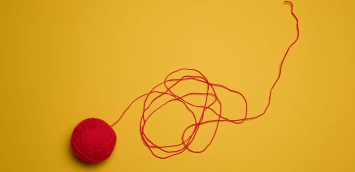 A ball of red woolen threads on a yellow background, top view