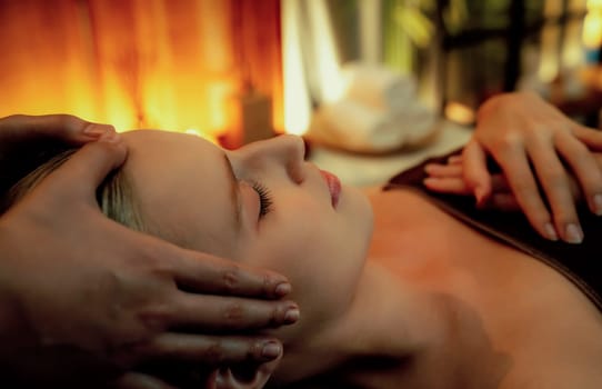 Caucasian woman enjoying relaxing anti-stress head massage and pampering facial beauty skin recreation leisure in warm candle lighting ambient salon spa in luxury resort or hotel. Quiescent