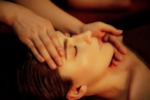 Closeup caucasian woman enjoying relaxing anti-stress head massage and pampering facial beauty skin recreation leisure in warm candle lighting ambient salon spa in luxury resort or hotel. Quiescent