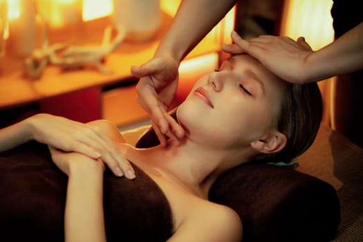 Caucasian woman enjoying relaxing anti-stress head massage and pampering facial beauty skin recreation leisure in warm candle lighting ambient salon spa in luxury resort or hotel. Quiescent