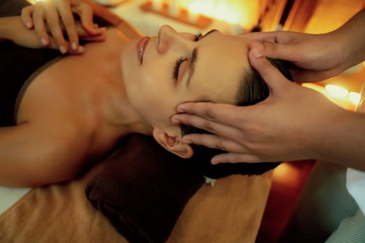 Closeup caucasian woman enjoying relaxing anti-stress head massage and pampering facial beauty skin recreation leisure in warm candle lighting ambient salon spa in luxury resort or hotel. Quiescent