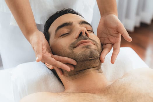 Caucasian man enjoying relaxing anti-stress head massage and pampering facial beauty skin recreation leisure in dayspa modern light ambient at luxury resort or hotel spa salon. Quiescent