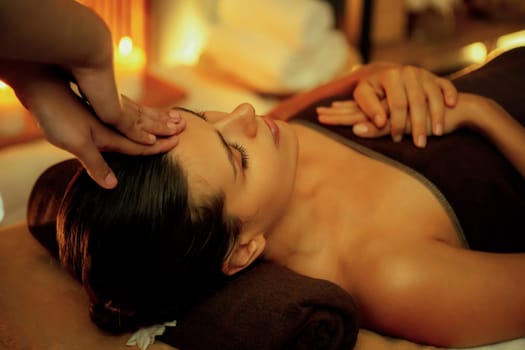 Caucasian woman enjoying relaxing anti-stress head massage and pampering facial beauty skin recreation leisure in warm candle lighting ambient salon spa in luxury resort or hotel. Quiescent
