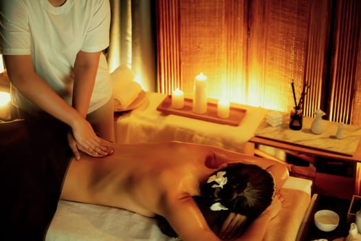 Caucasian woman customer enjoying relaxing anti-stress spa massage and pampering with beauty skin recreation leisure in warm candle lighting ambient salon spa at luxury resort or hotel. Quiescent