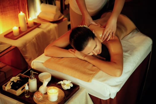 Caucasian woman customer enjoying relaxing anti-stress spa massage and pampering with beauty skin recreation leisure in warm candle lighting ambient salon spa at luxury resort or hotel. Quiescent