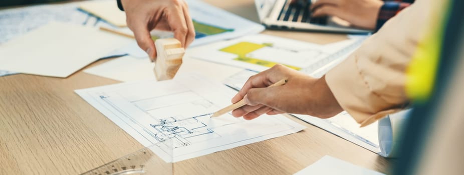 Skilled architect team using architectural equipment during colleague discussion about building design at meeting table with blueprint scatter around. Closeup. Focus on hand. Delineation.