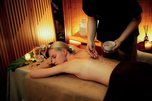 Woman customer having exfoliation treatment in luxury spa salon with warmth candle light ambient. Salt scrub beauty treatment in Health spa body scrub. Quiescent