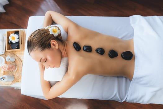 Panorama top view hot stone massage at spa salon in luxury resort with day light serenity ambient, blissful woman customer enjoying spa basalt stone massage glide over body. Quiescent