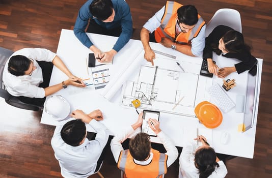 Top view banner of diverse group of civil engineer and client working together on architectural project, reviewing construction plan and building blueprint at meeting table. Prudent