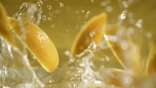 Close up of fresh lemon dropping in to water and separated in to sliced lemon at separated yellow background with making water wave and splashing water. Freshness and vitality concept. Macro. Pabulum.