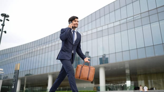 Smart business man using phone to talking while walking at building. Happy manager walking at street while talking on smart phone to discuss business plan or marketing strategy or working. Exultant.