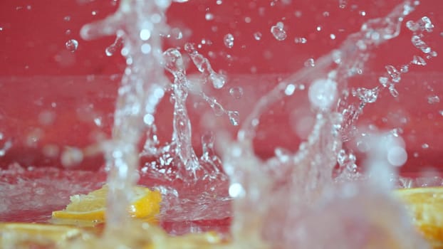 Close up of fresh lemon slices splashing on red background. Macro of sliced lemon dropping and falling in to splashing water. Freshness and hydration concept. Citrus. Design for poster. Pabulum.