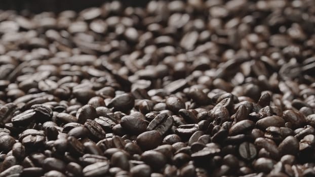Macro shot of super slow motion shot of fresh coffee bean placed with black background. Close up of piles of aromatic roasted coffee seed surrounded. Macrography. Beans scattering around. Comestible.