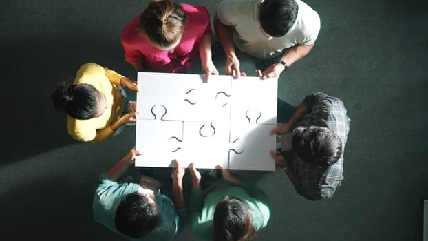 Top down view of business people gathering jigsaw together at meeting. Aerial view of diverse team collect or put piece of jigsaw puzzle together and standing while wearing casual cloth. Symposium.