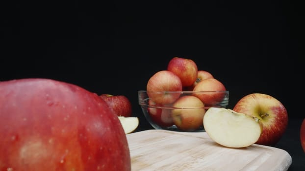 Macrography of apples displayed in various forms: whole, sliced, and within a glass bowl with black background. Each close-up shot captures the red colors of the apples on cutting board. Comestible.