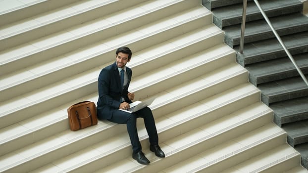 Top view of investor working or planing strategy by using laptop at stair. Professional business man wearing suit while working and typing data analysis by using laptop at modern hotel. Exultant.