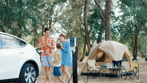 Outdoor adventure and family vacation camping in nature travel by eco friendly car for sustainable future. Lovely family recharge EV car with EV charging station in campsite. Perpetual