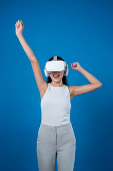 Smart female standing with blue background wearing VR headset connecting metaverse, futuristic cyberspace community technology. Elegant woman excited seeing generated virtual scenery. Hallucination.