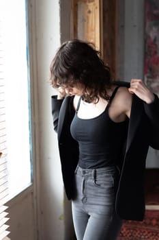 young beautiful woman posing in the studio, standing in black clothes near the window