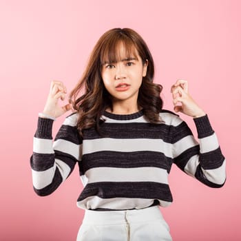 Asian happy portrait beautiful cute young woman standing angry and mad raising fist frustrated and furious while shouting with anger isolated, studio shot on pink background and copy space