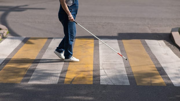 Close-up of the legs of a blind woman crossing the road at a crosswalk with a cane