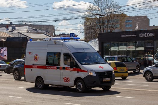 white ambulance minibus driving along city street at sunny day in Tula, Russia - June 7, 2021