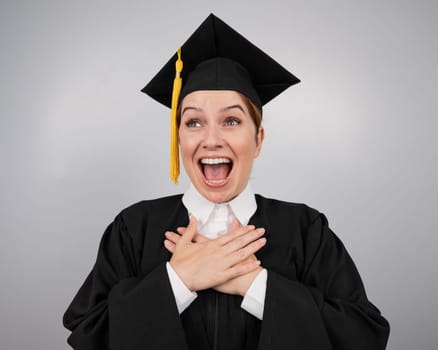 Caucasian woman in graduate gown dreamily holds her hands on her chest