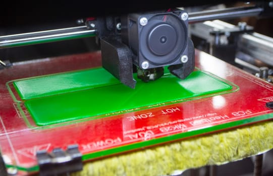 3D printer close up. A working 3D printer in process of printing object from molten plastic. 3D printer creating model by flowing liquid plastic from an extruder of printer. 3D printing technology