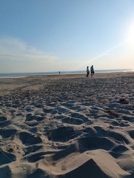 Two people couple walking together in the beach sunlight seashore. High quality photo. Mobile vertical photo