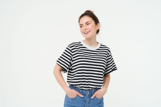 Image of young confident woman in casual outfit, looking happy, standing against white background.