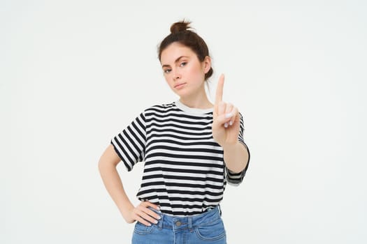 Image of confident woman, shows one finger, taboo, stop gesture, disapprove smth, gives warning, stands over white background.