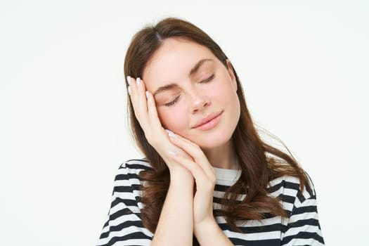 Close up portrait of tender, smiling young woman, closes her eyes and touches her palm, sleeping on her hand, isolated on white background.