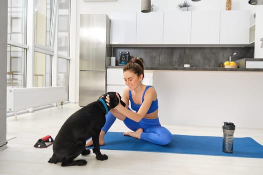 Portrait of smiling, beautiful woman doing sports, workout from home with her black dog, doing sports in living room.