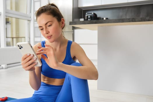 Young sportswoman looks with interest at smartphone screen, reading on mobile phone. Sport and wellbeing concept