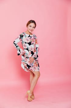 woman in a beautiful floral dress stands on a pink background