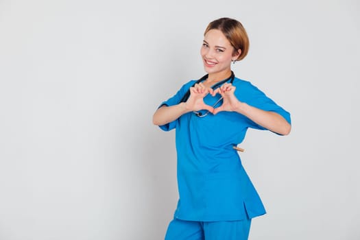 woman doctor in surgical suit with phonendoscope shows heart with hands