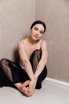 fashionable woman in black pants sits in a corner on the floor