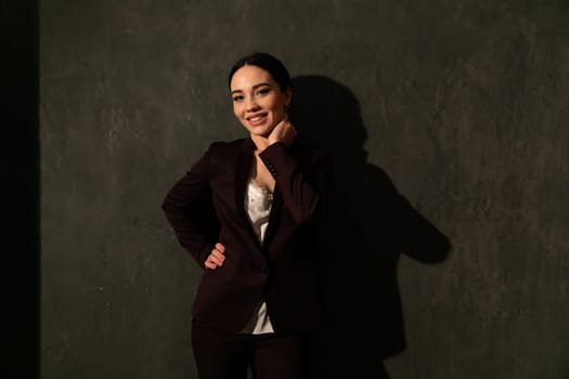 woman in a business suit stands against a black wall in the shadows