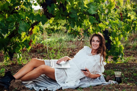 woman with glass of wine and a laptop in the vineyard